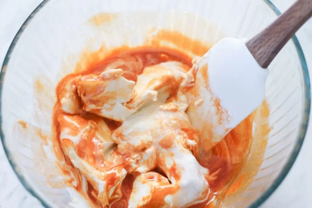 Clear bowl with spatula mixing together cream cheese, buffalo sauce and ranch.