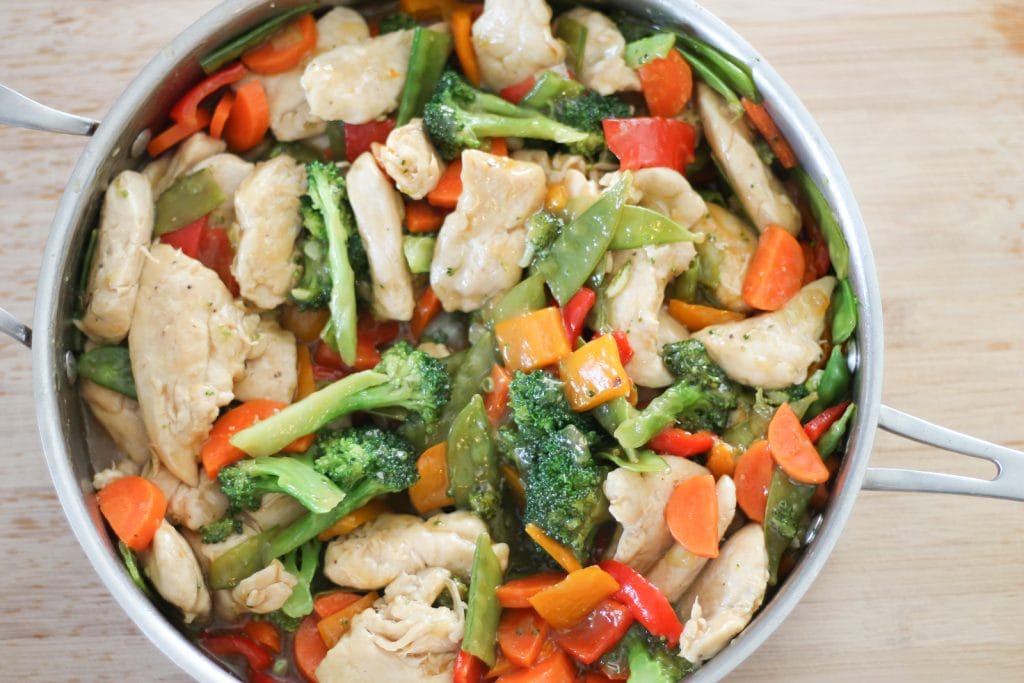 Finished chicken stir-fry in pan on a wooden cutting board. 