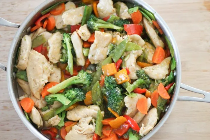 Finished chicken stir-fry in pan on a wooden cutting board.