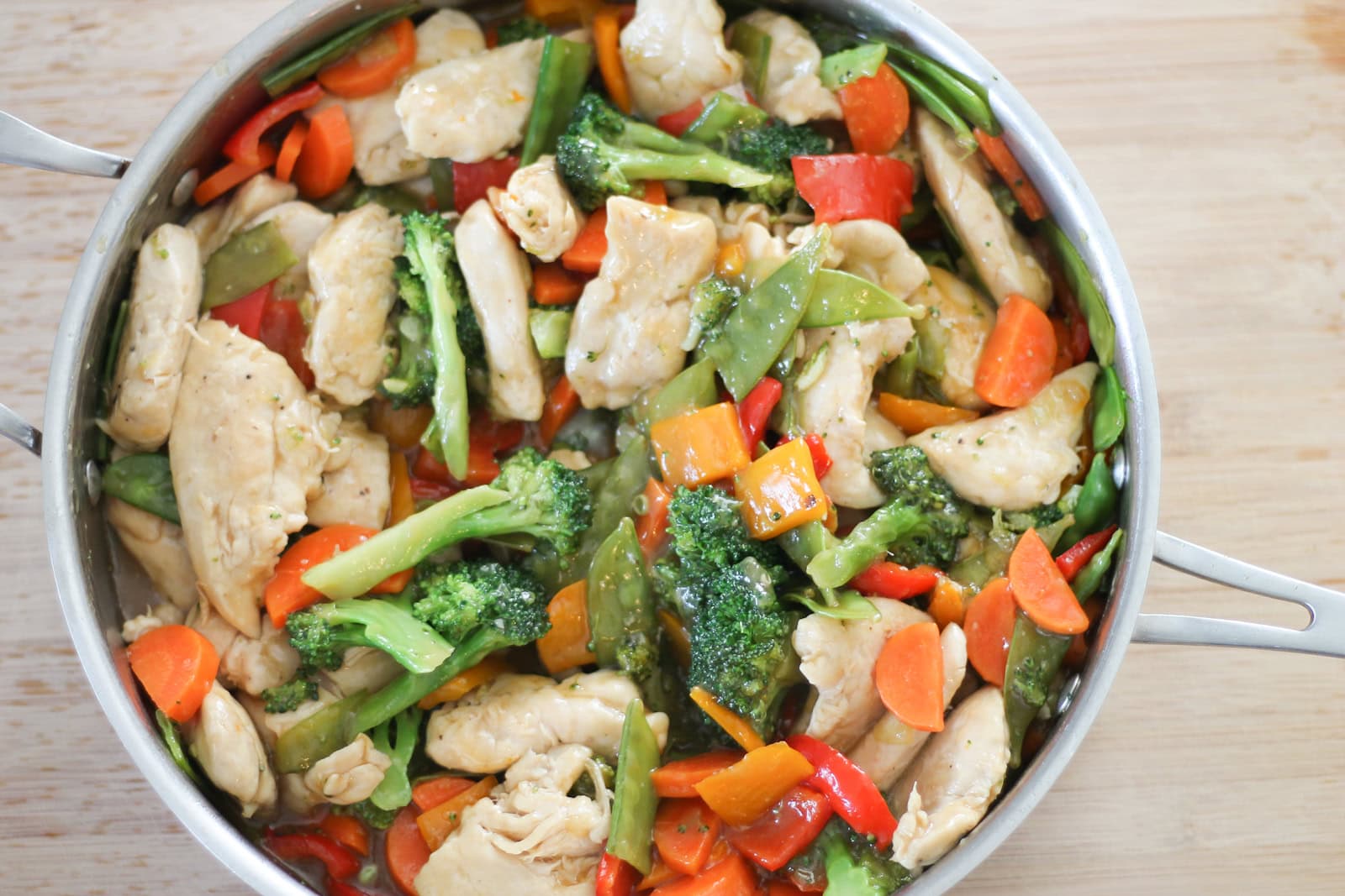 Finished chicken stir-fry in pan on a wooden cutting board.